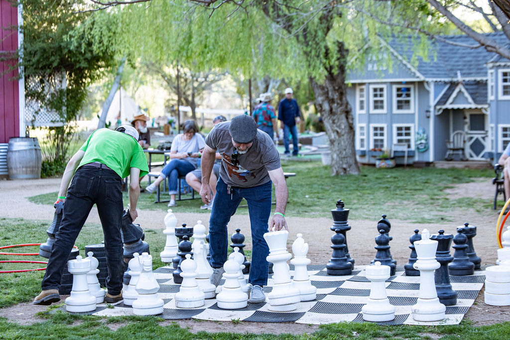 Two people playing oversized outdoor chess on a board in a park.