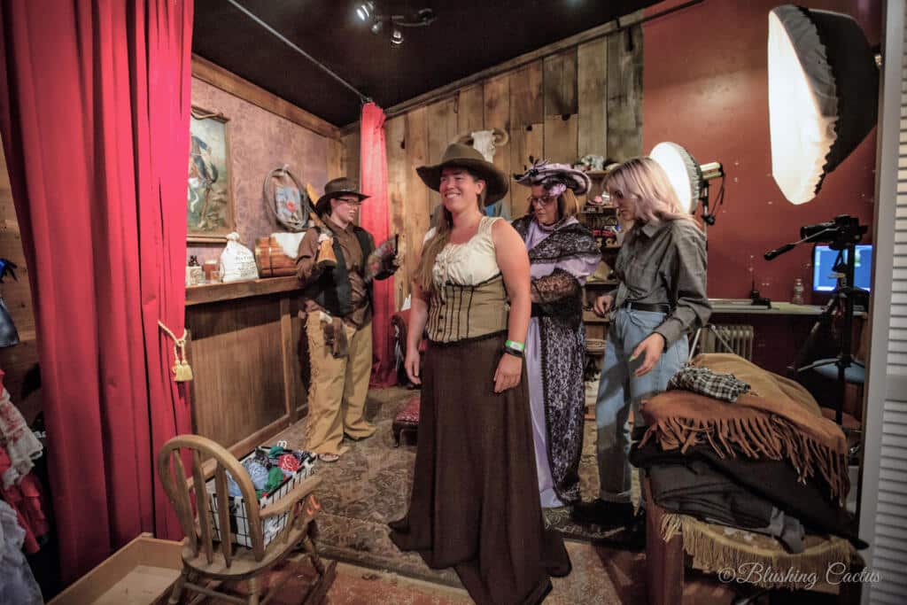 Four people roleplaying in a western-themed saloon setting with costumes and props.