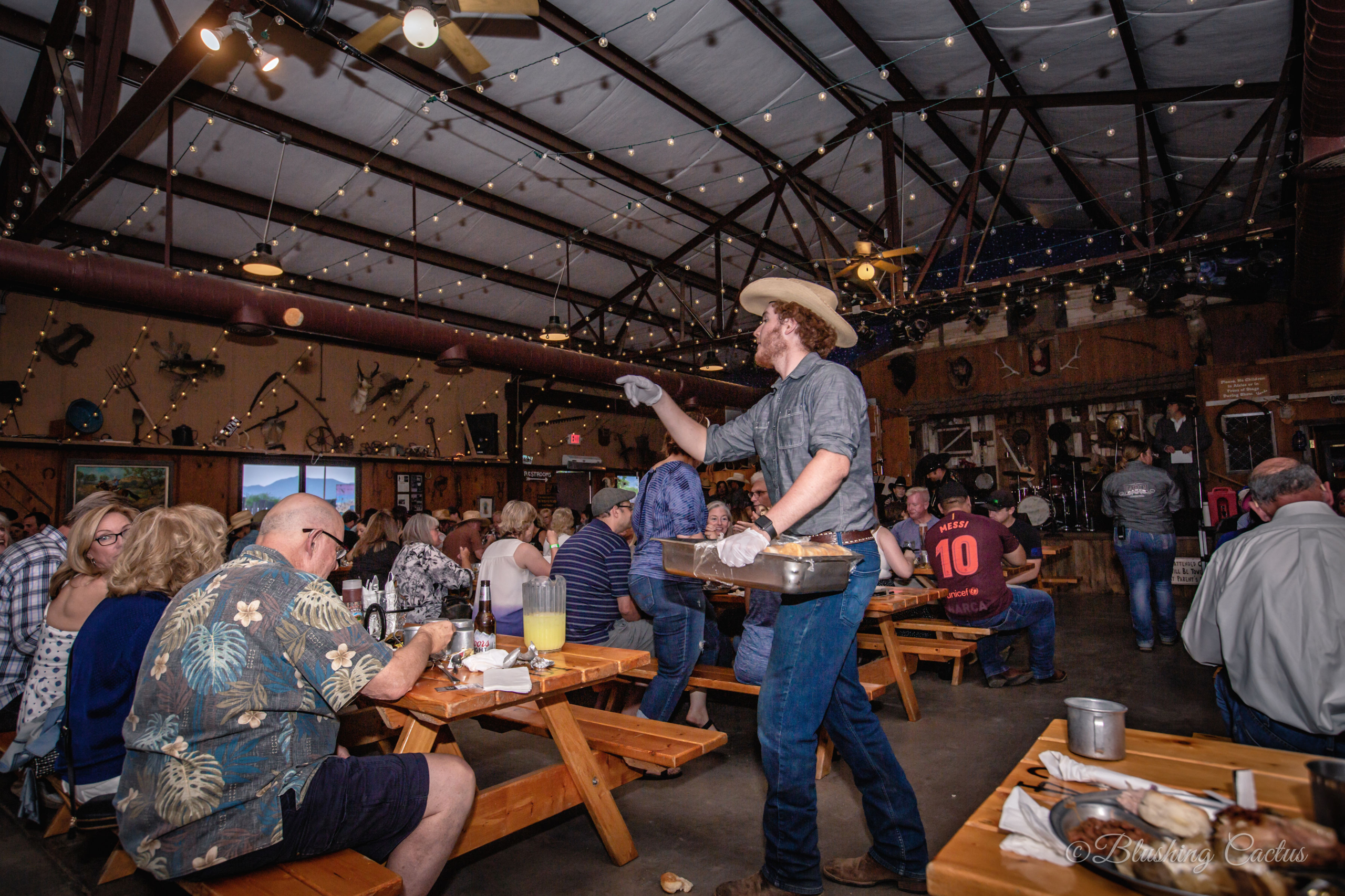 Cowboy serving food to guests at a lively rustic-themed restaurant event.