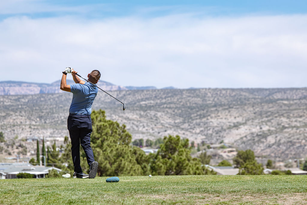 Golfer taking a swing on a scenic hilltop golf course.