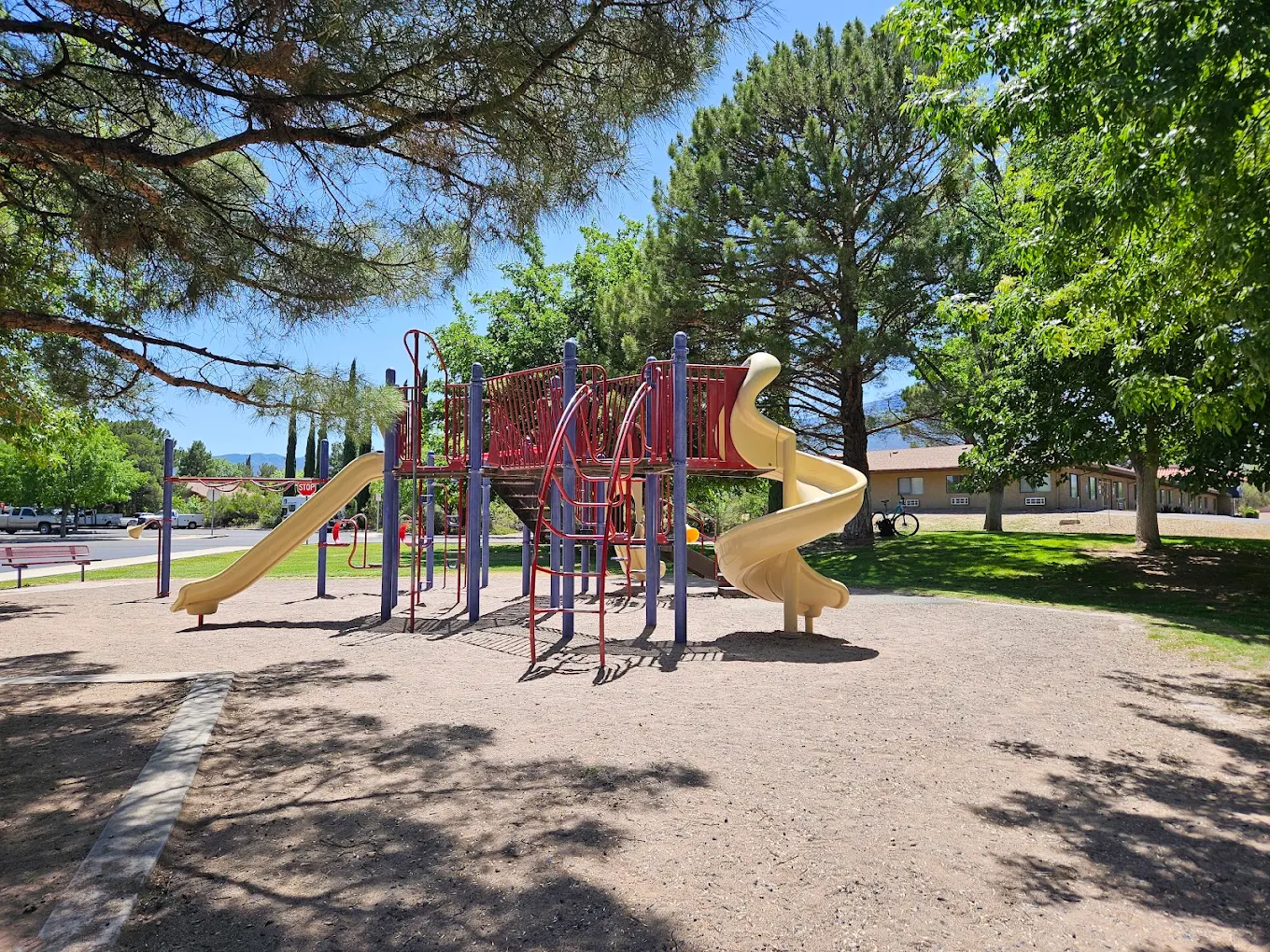 Colorful playground with slides, climbers, and swings in a shaded park area