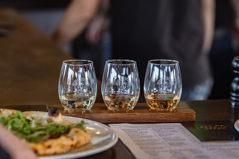Three wine glasses with different wines, wooden board, salad plate, wine menu.
