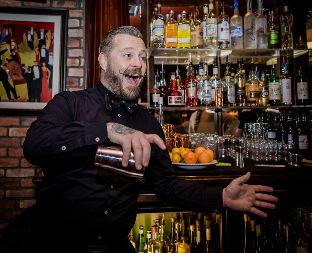 Bartender mixing drink behind bar with bottles and oranges.