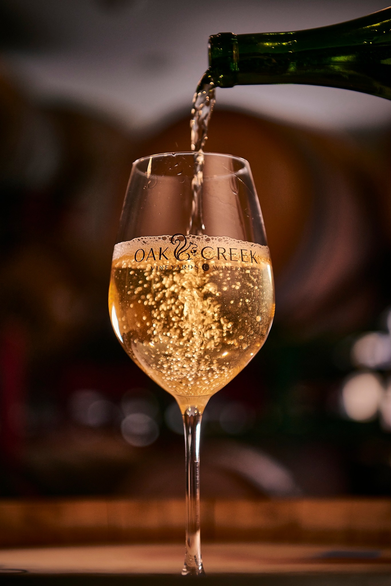 Sparkling white wine being poured from bottle into glass, Oak & Creek Vineyards.