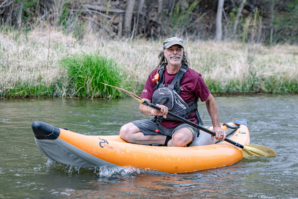 Smiling man kayaking with fishing rod in calm river surrounded by greenery