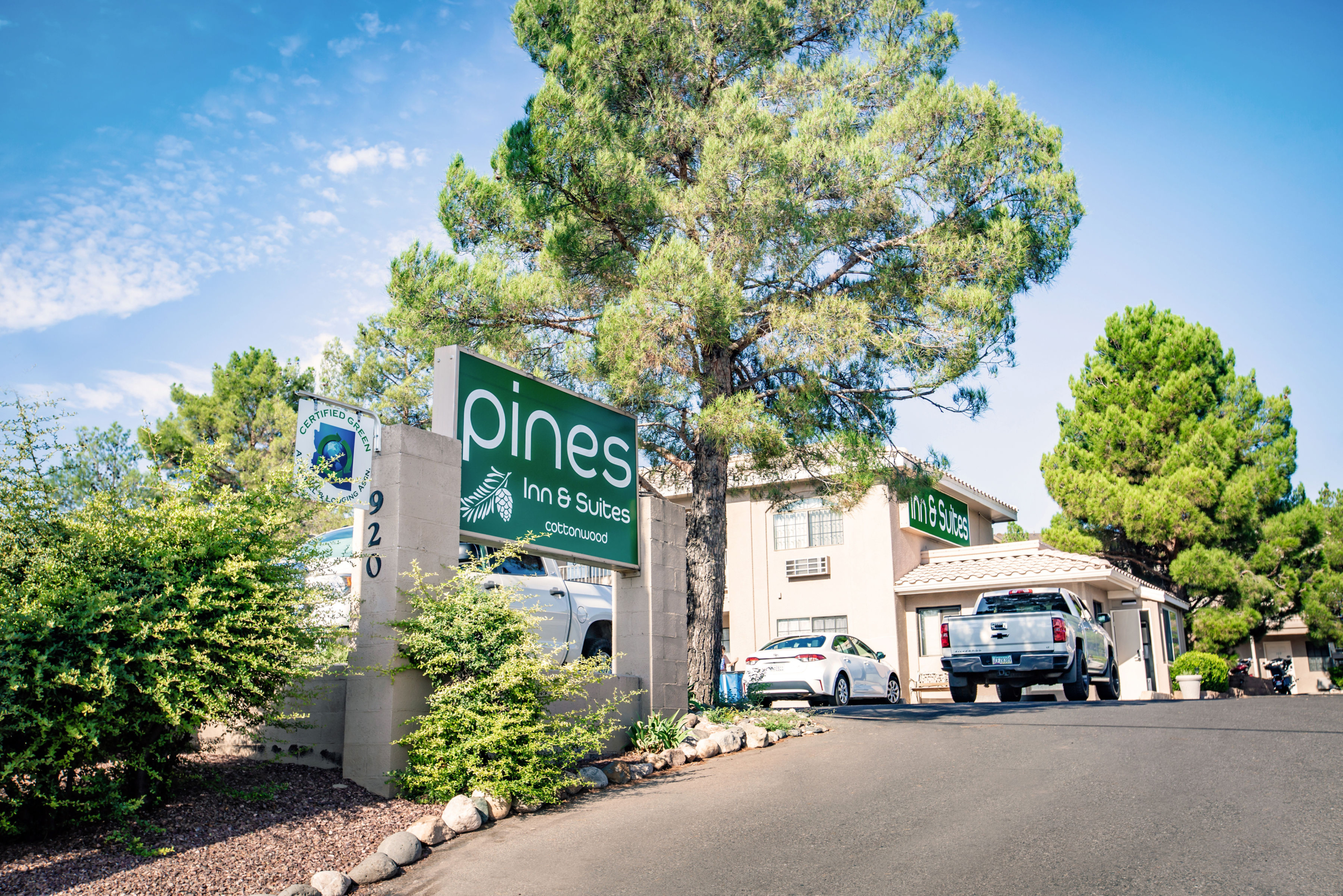 Pines Inn & Suites Cottonwood entrance with parked vehicles and green trees
