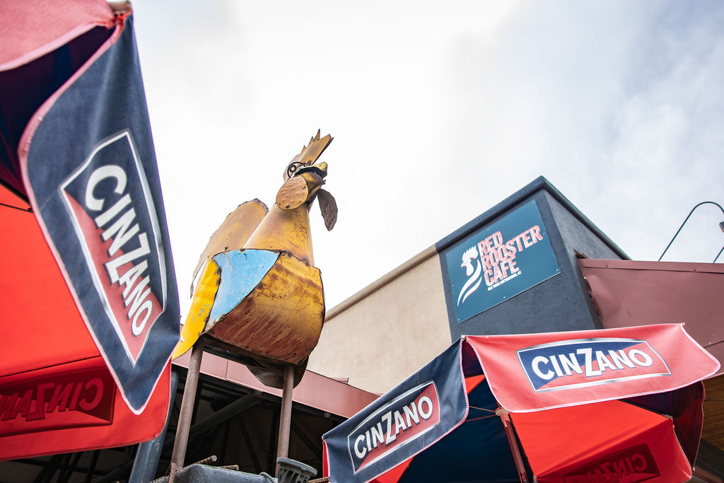 Colorful rooster statue with Cinzano flags and Red Rooster Cafe sign