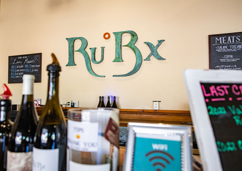 RuBx restaurant bar featuring wine bottles, menu boards, and signage for live music and meats.