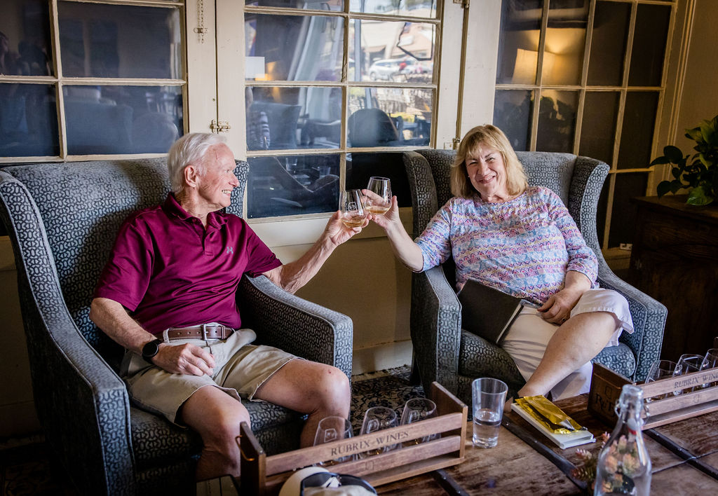 Smiling elderly couple clinking wine glasses in cozy room