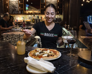 Smiling server adding cheese to pizza at Bocce pizzeria and patio bar.