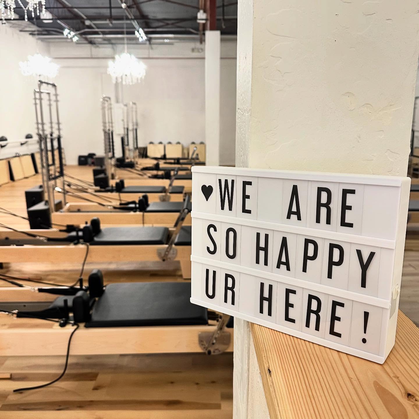 Pilates studio open sign with happy message and exercise equipment in background.