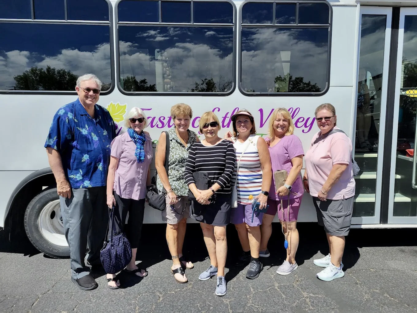 Six smiling adults posing together near a tour bus labeled 'Fascinating Valley Tours'