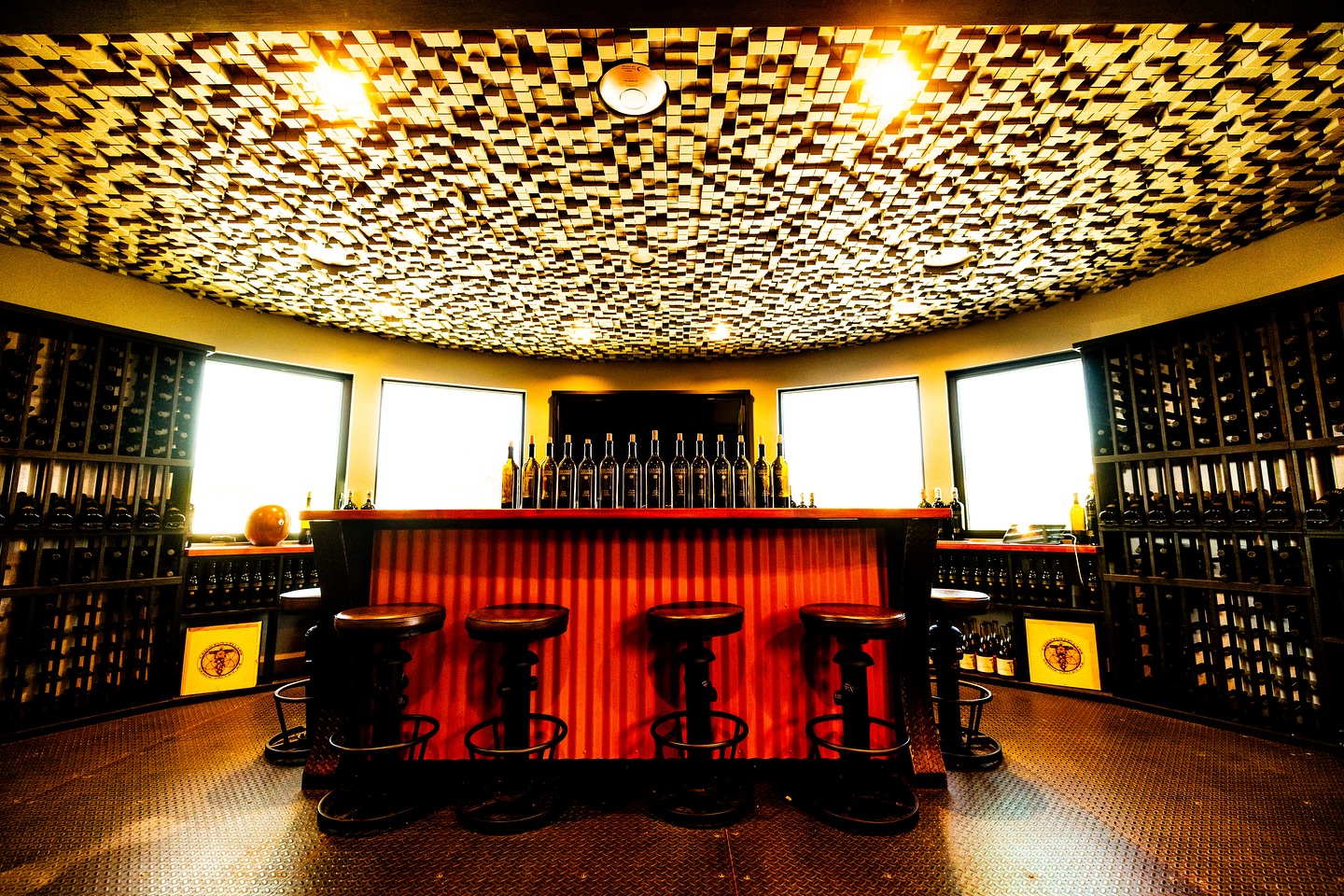 Elegant wine bar with illuminated ceiling, bar stools, and shelves of wine bottles.