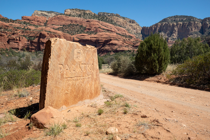 Stone marker indicating Palatin Trailhead in desert landscape with red rock formations.