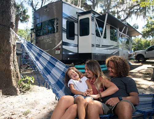 Family relaxing on hammock near North Point RV in a sunny campsite.