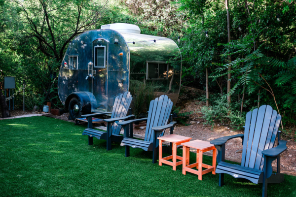 Vintage Airstream trailer in a lush garden setting with Adirondack chairs and small tables.