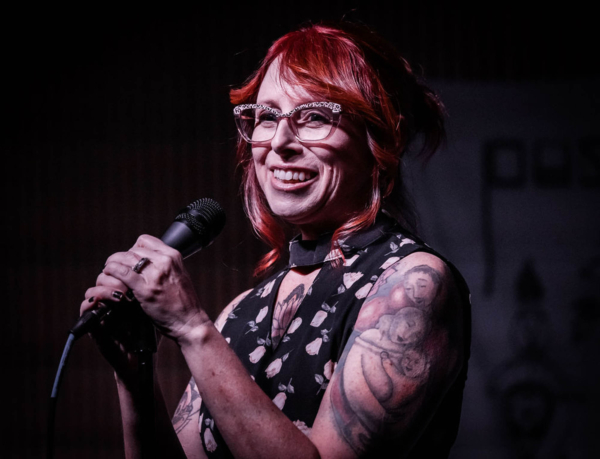 Smiling person with red hair performing on stage holding microphone