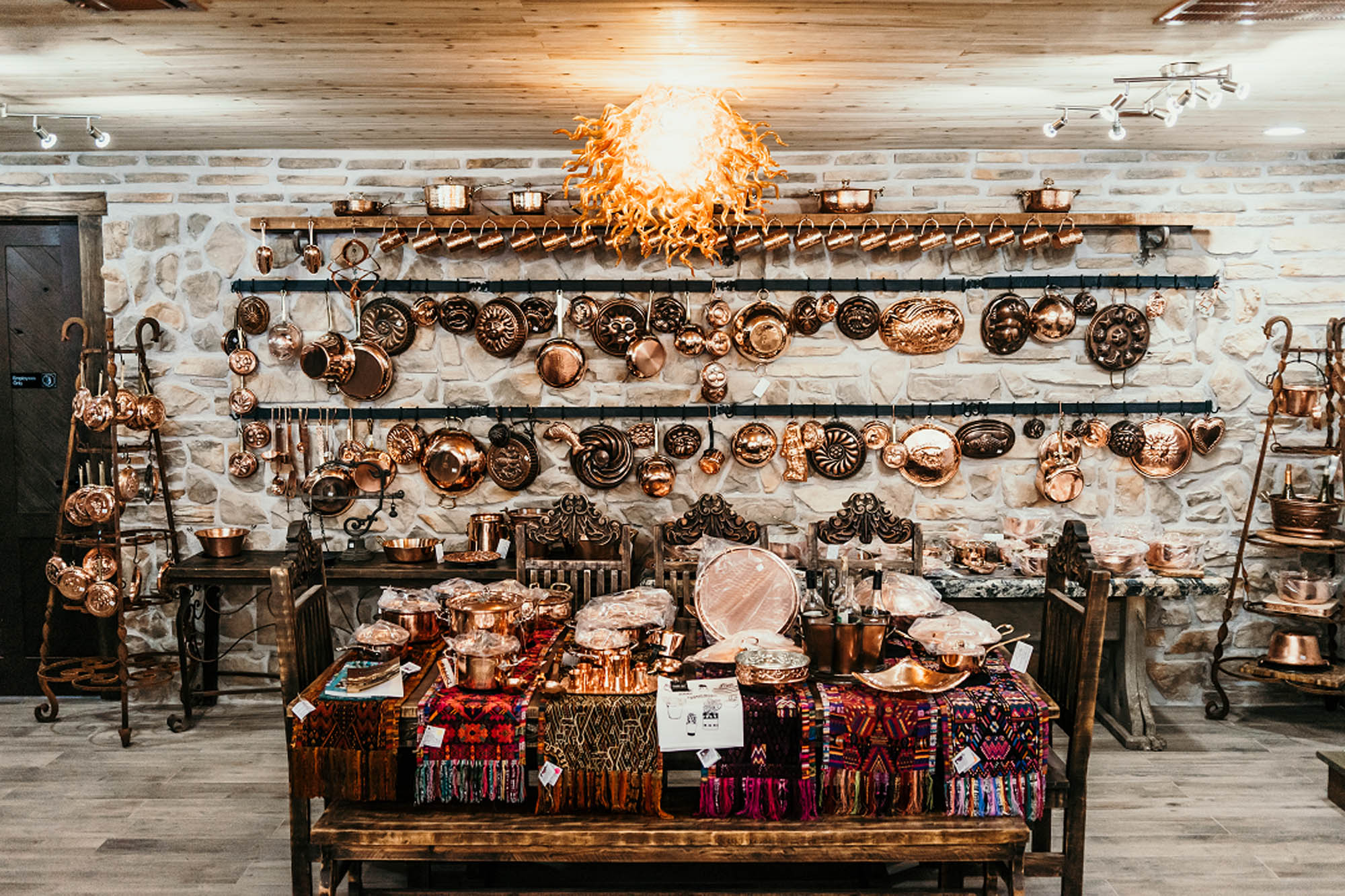 Vintage copper cookware and textiles displayed on rustic shelves in warm-lit store.
