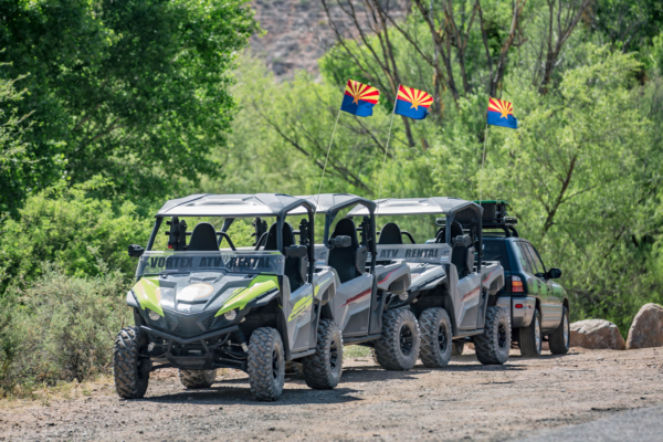 Three ATV rentals on a forest trail with Arizona state flags flying.