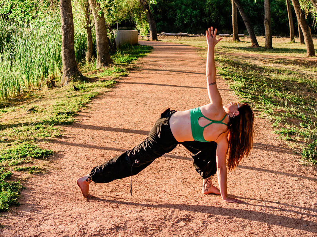 Woman performing side plank yoga pose outdoors in park.