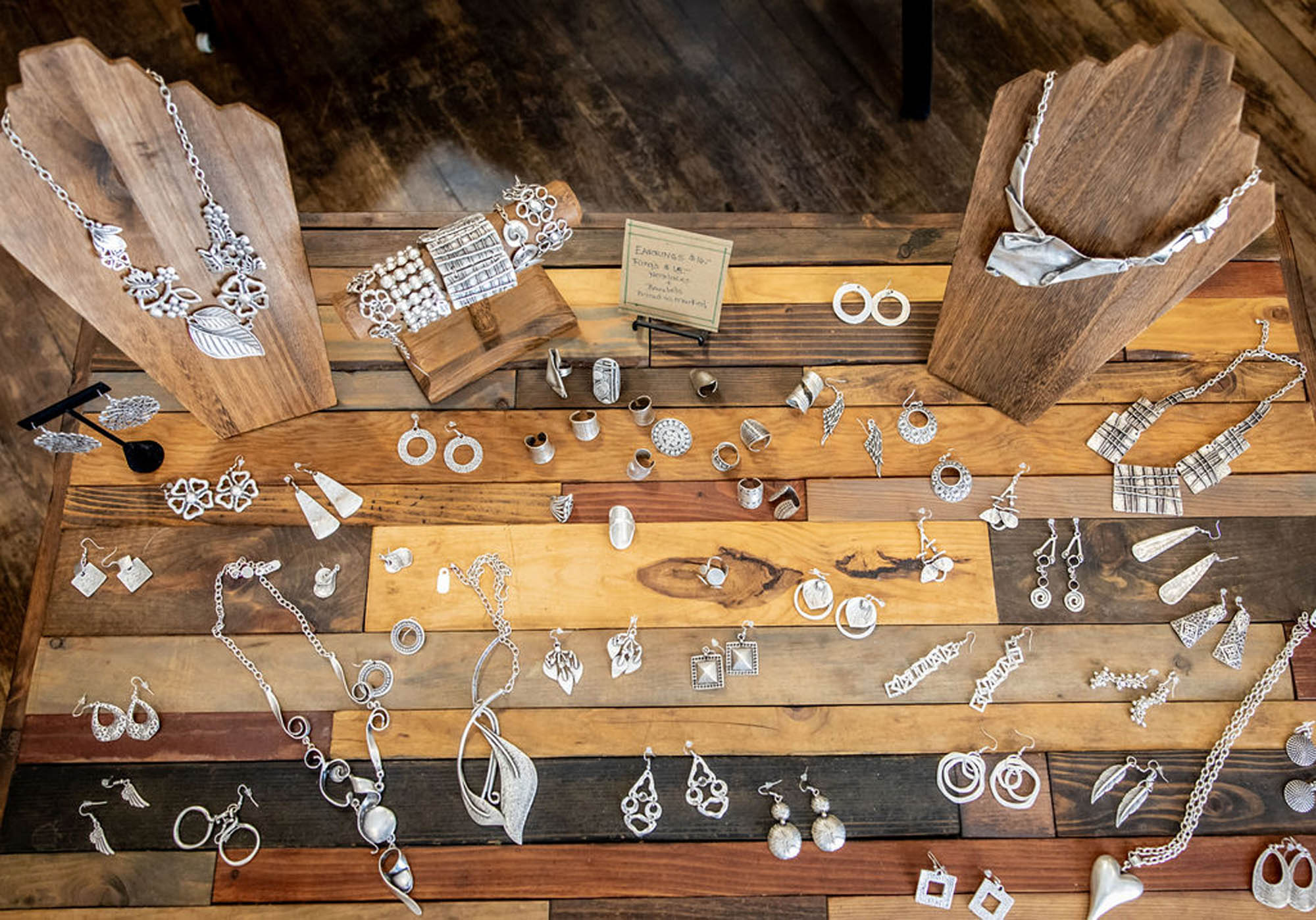 Handcrafted silver jewelry display with necklaces, earrings, rings on wooden planks.