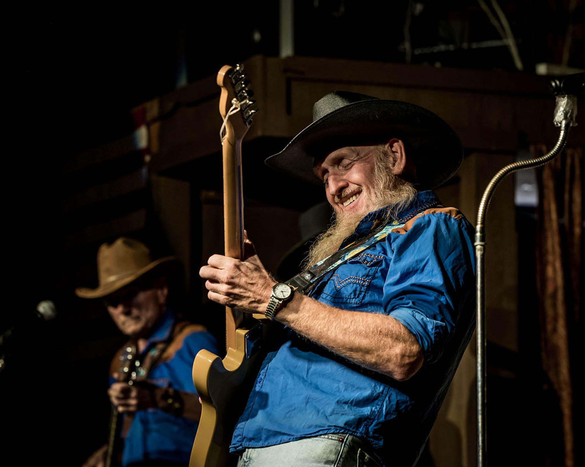 Smiling musician playing electric guitar on stage with cowboy hat