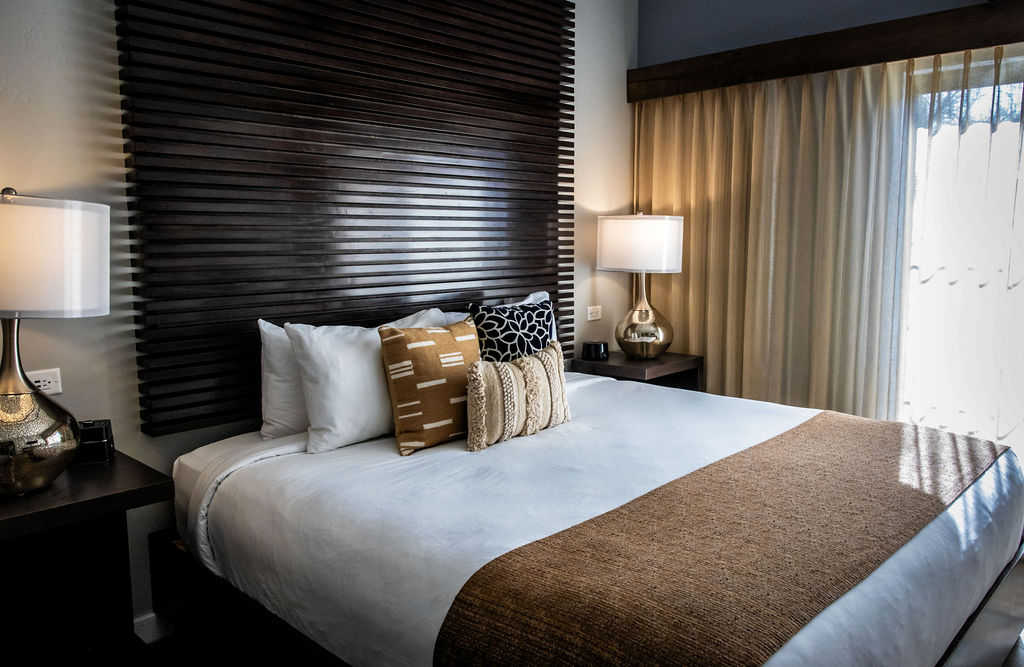 Modern hotel room with neatly made bed, lamps, and sliding glass door view.