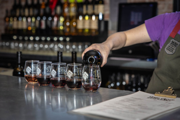 Bartender pouring dark liquids into small wine glasses for tasting.