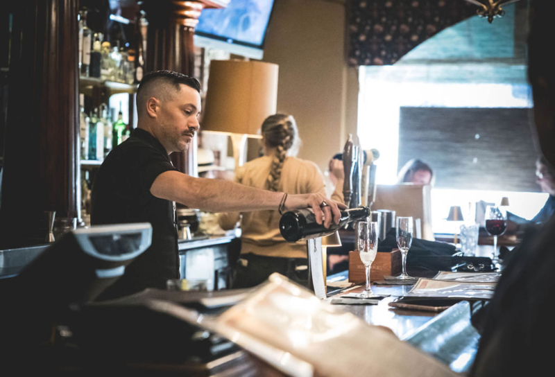 Bartender pouring wine into glass at busy bar counter.