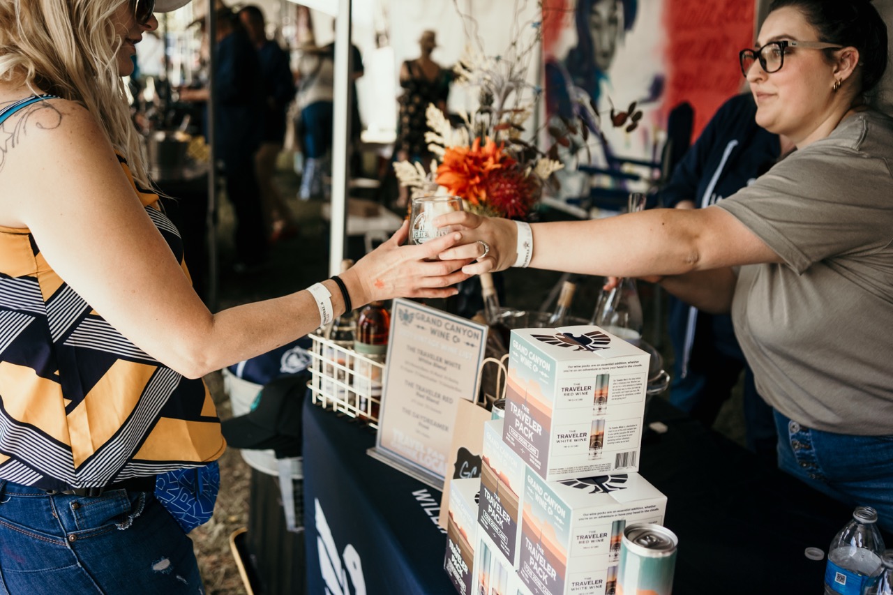Two people exchanging wine samples at a Grand Canyon Wine Co. booth.