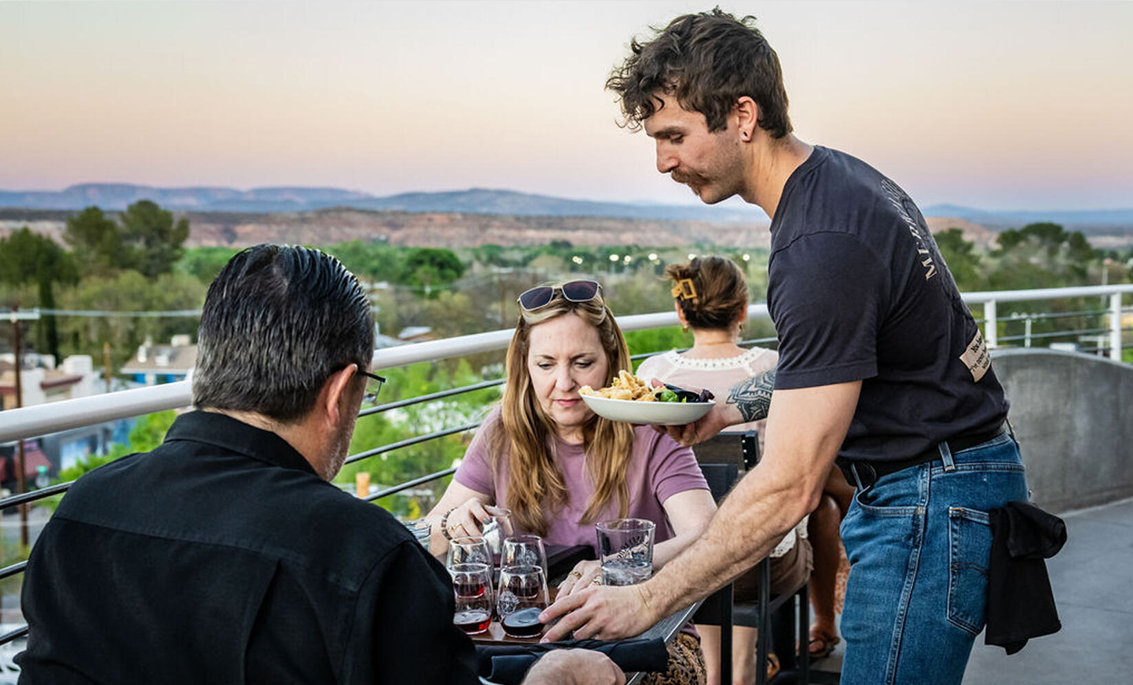 Group enjoying drinks and food on rooftop patio at sunset