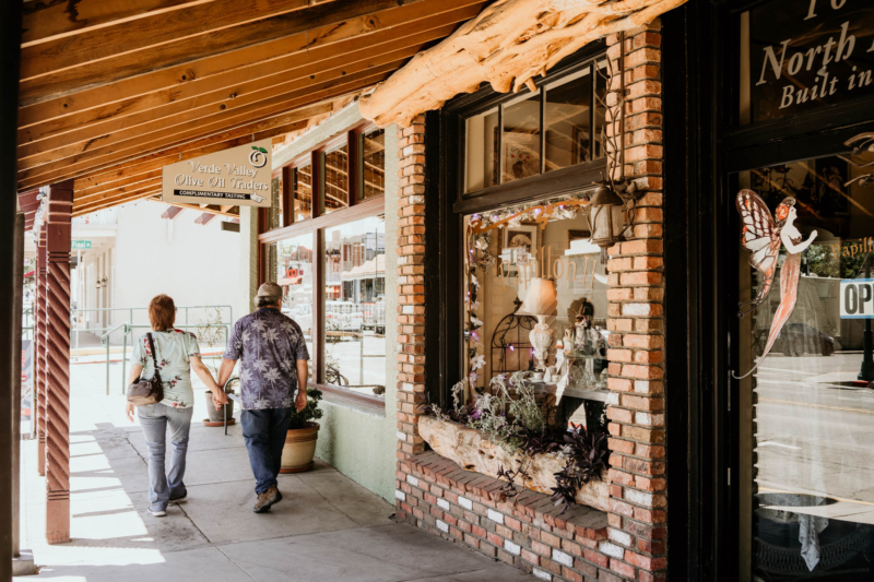 Couple walking past storefronts with brick walls and window displays in small town.