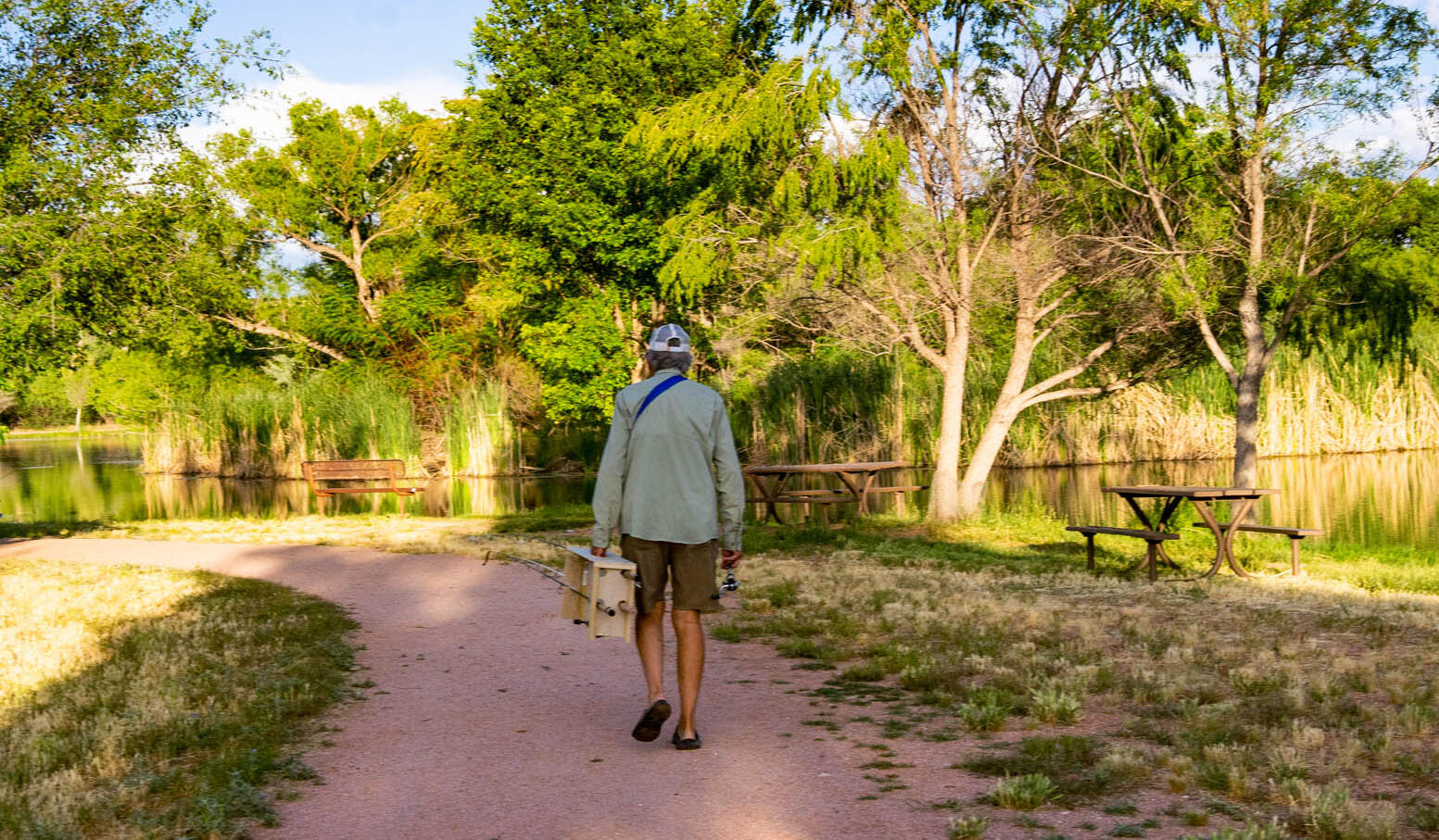 Person walking on paved trail near serene lake with picnic tables