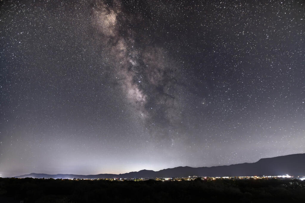 Milky Way galaxy over a dark landscape with distant lights.