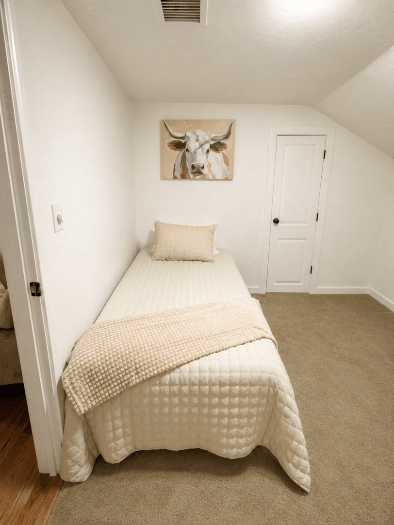 Cozy single bed beneath cow painting in small bedroom