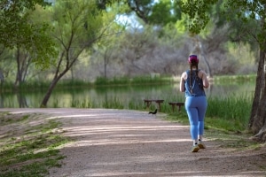 Woman with braided hair jogs on a park trail beside a lake.